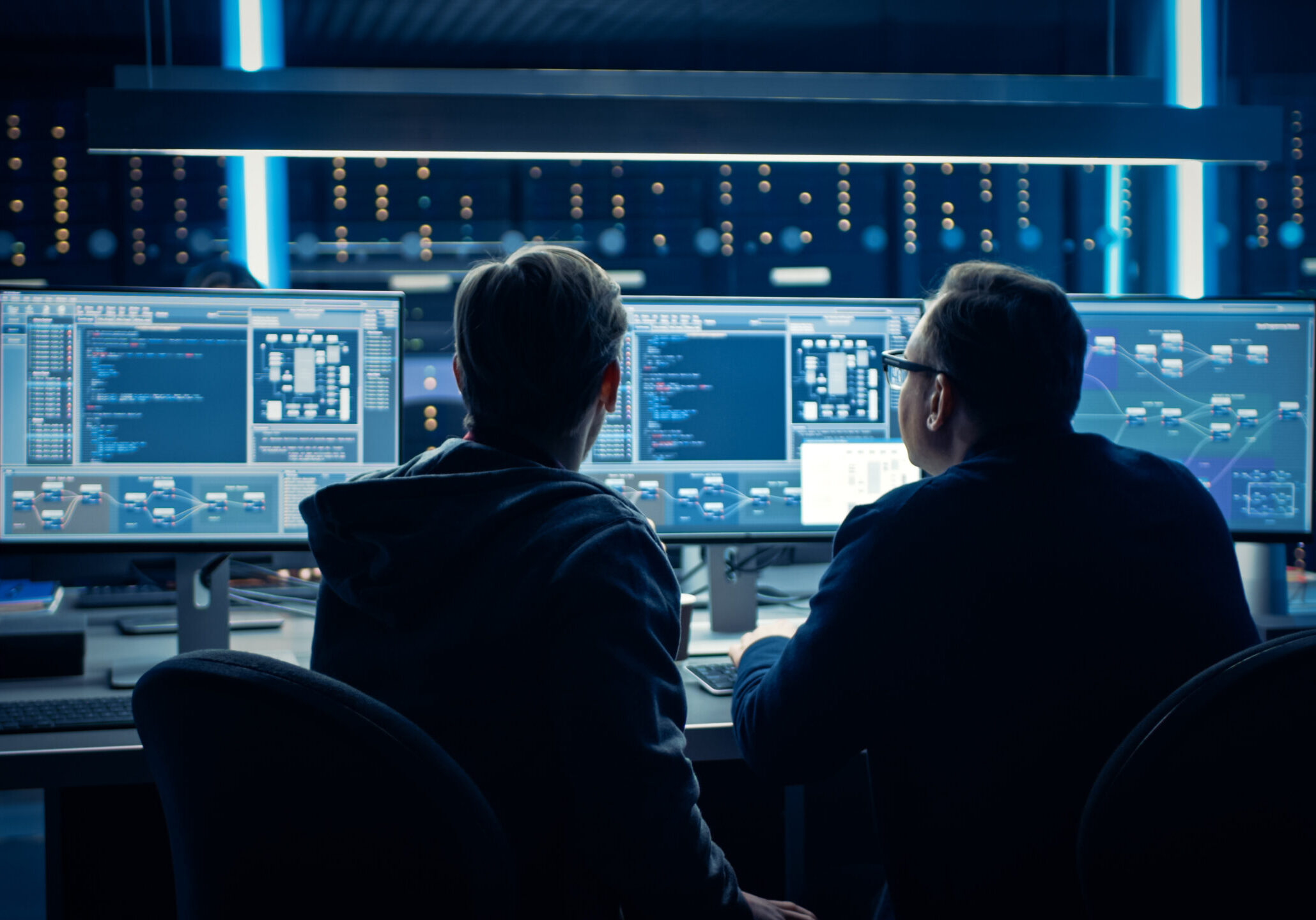 Two Professional IT Programers Discussing Blockchain Data Network Architecture Design and Development Shown on Desktop Computer Display. Working Data Center Technical Department with Server Racks